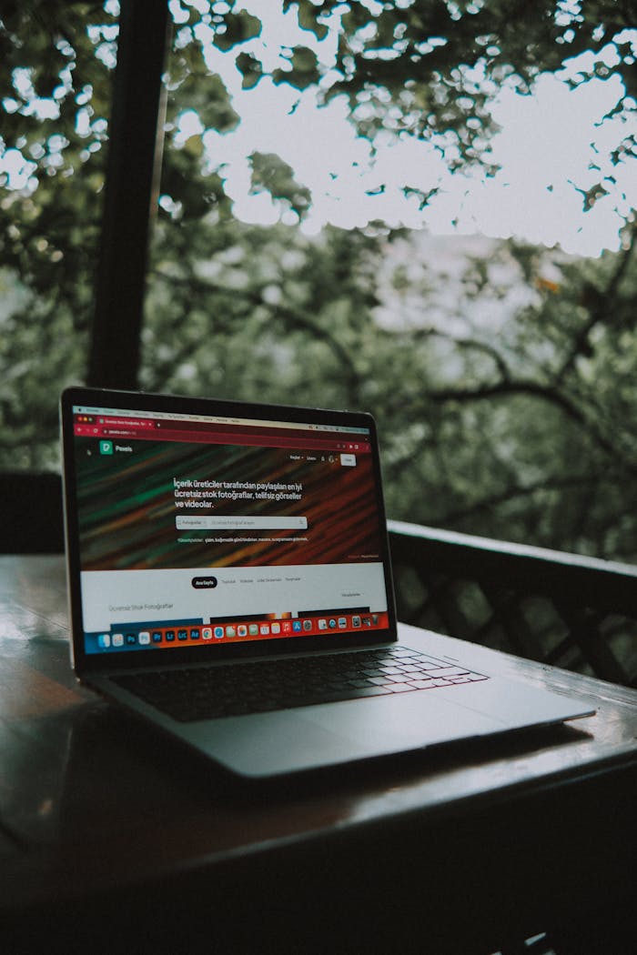 Home Open laptop showing a website screen on a wooden table in an outdoor terrace setting.