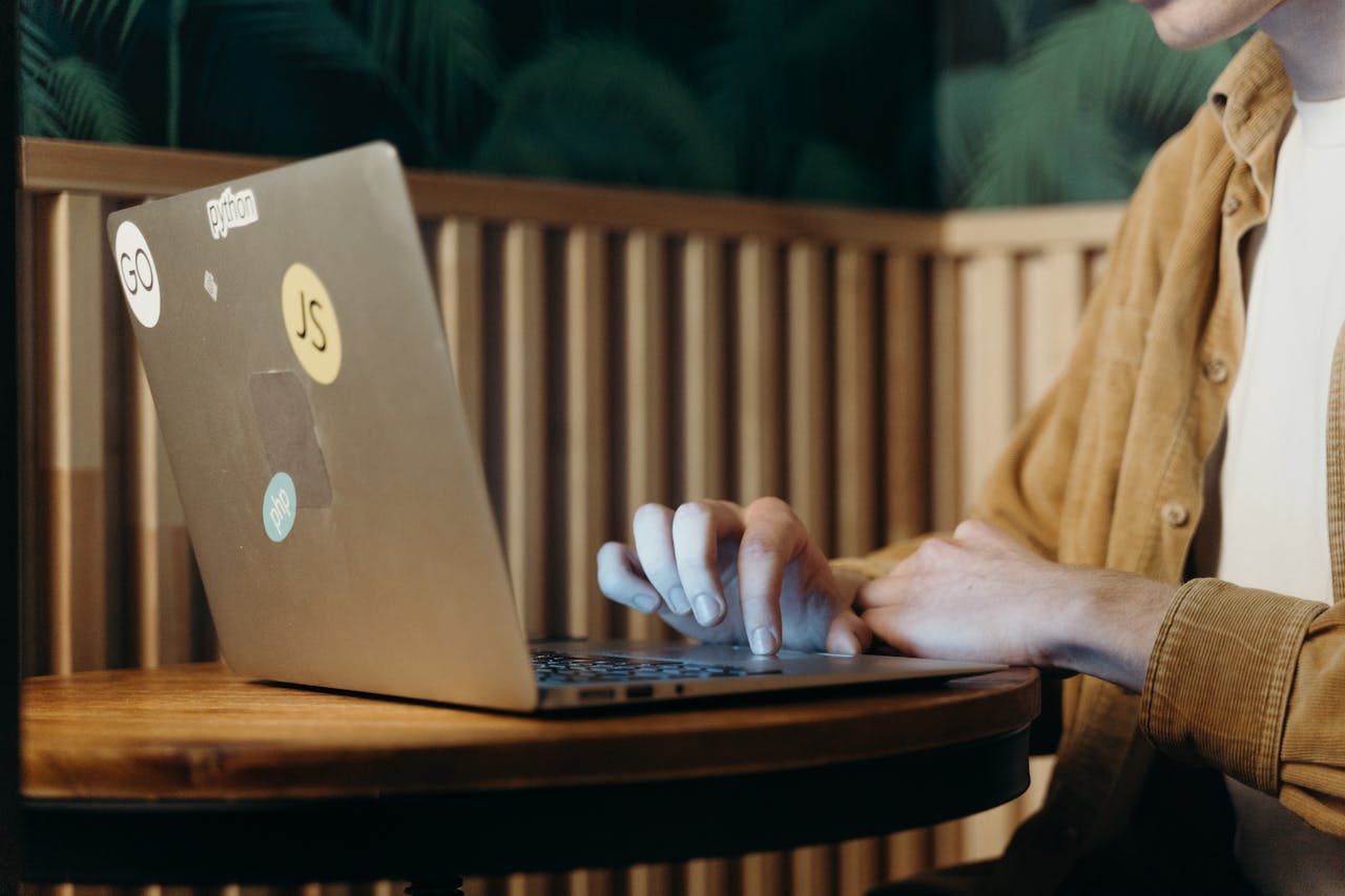 Home Person typing on a laptop in a cozy café, surrounded by greenery, enhancing focus and productivity.